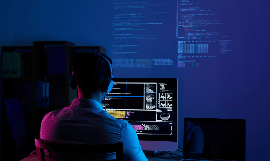 Software developer coding on multiple monitors in a dark office environment