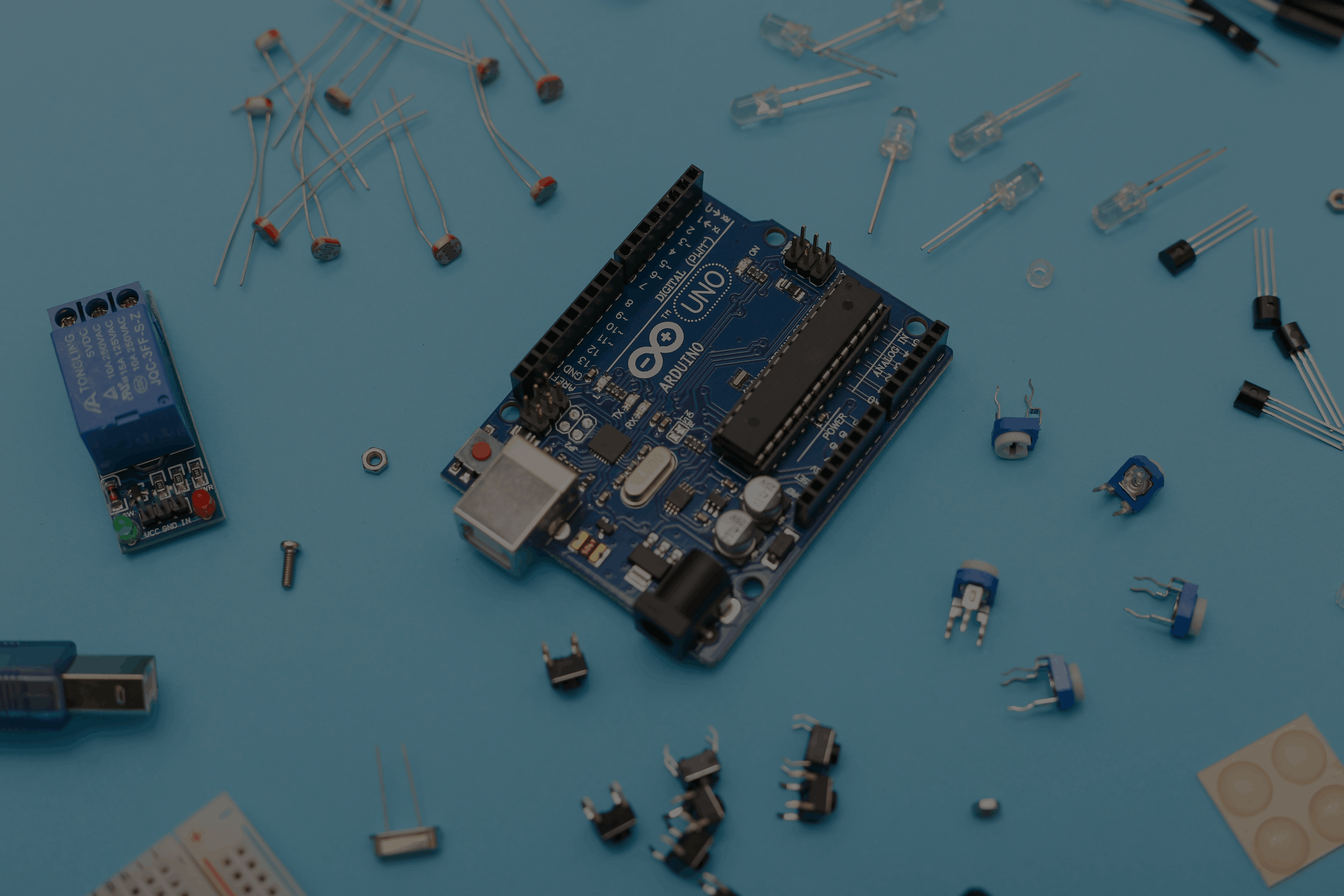 Assortment of electronic components and an Arduino board on a blue surface, representing electronics and hardware projects.