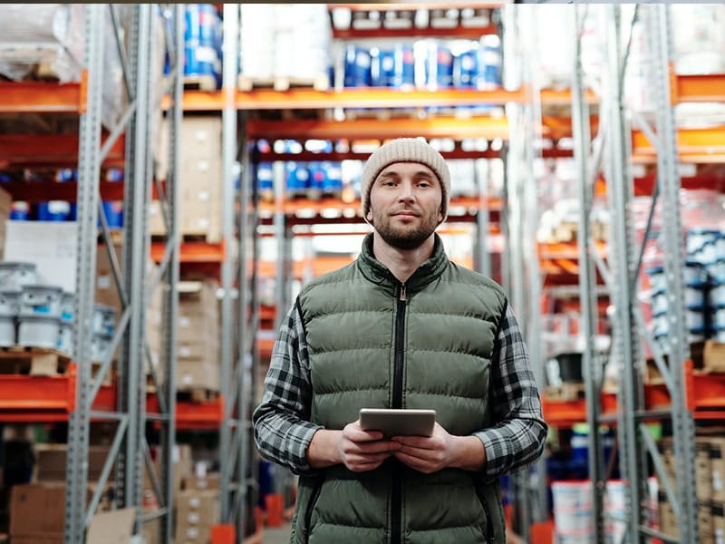 Warehouse worker holding a tablet inside a storage facility with shelves